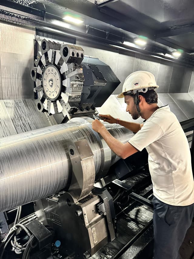 An operator gauging a journal on a CNC lathe mid-cut.