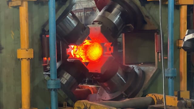 The four dies of the radial forge closing on a billet at forging heat.