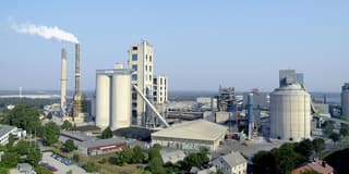 An aerial view of a cement plant: kilns, a preheater tower and storage silos under a clear sky.