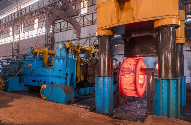 A forging manipulator holding a glowing workpiece to the press.
