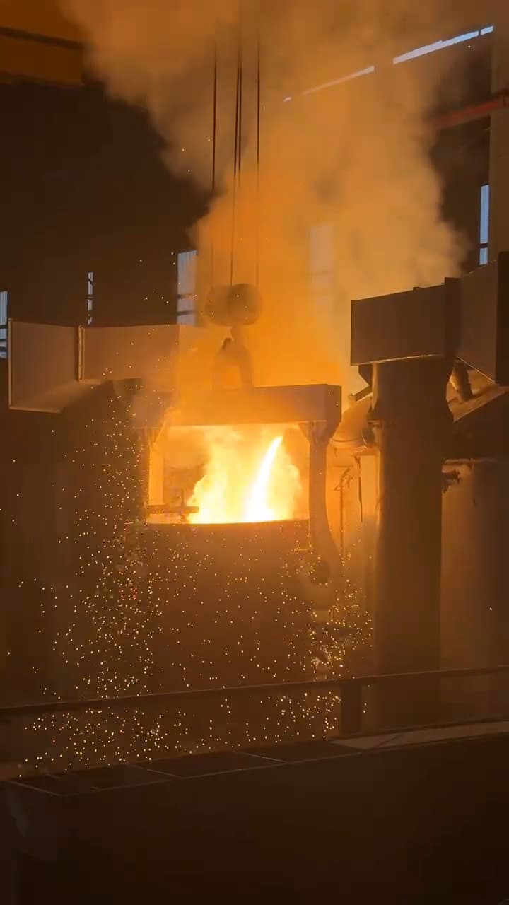 Molten steel pouring from the furnace into the mould, sparks rising.
