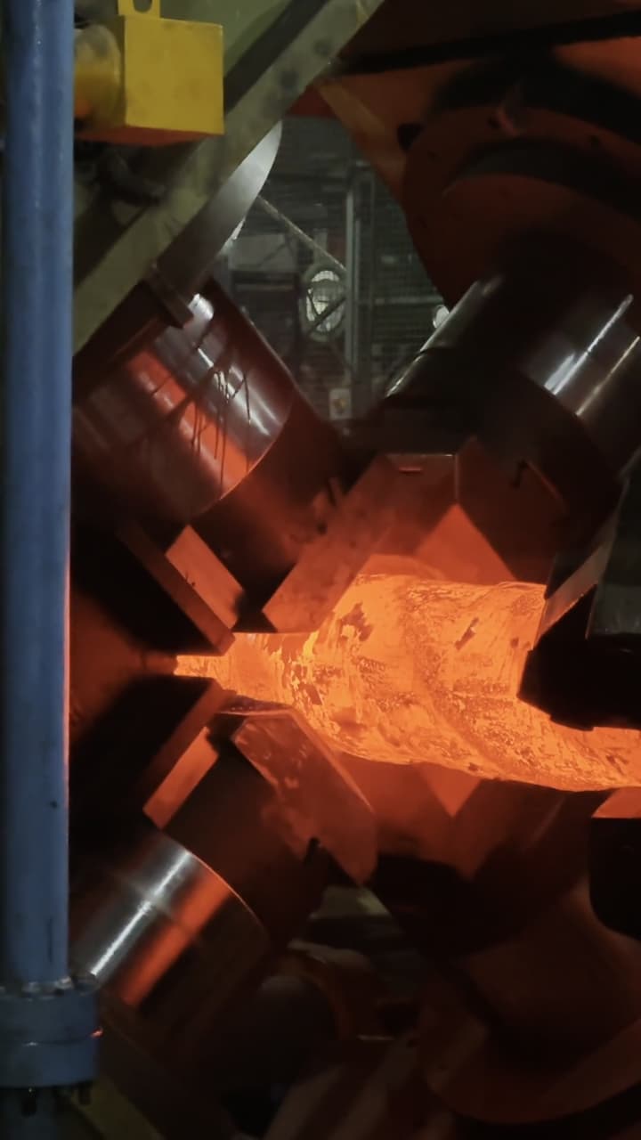 The radial forge working a glowing billet, seen from the shop floor.