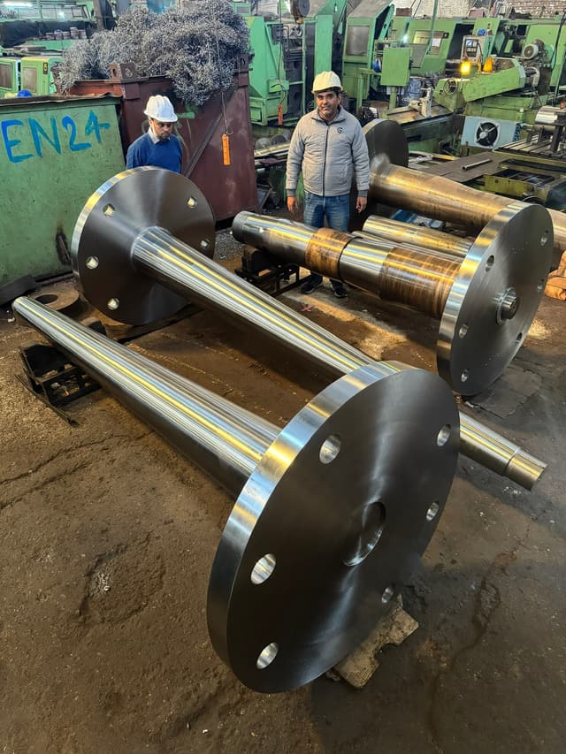 Rudder shafts with integral flanges laid out on the shop floor, the grade chalked on the end.