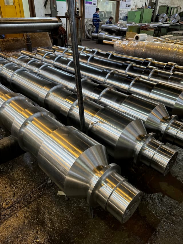 A row of machined steel mill shafts stacked on timbers.